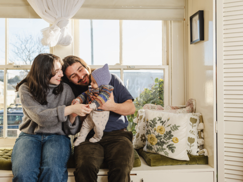 Happy family sitting together near windows inside brightly lit home - Australian Stock Image