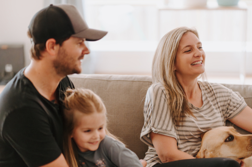 Happy family snuggles on the couch with their pet dog - Australian Stock Image