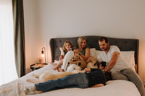 Happy family snuggling in a cosy bedroom with their dogs - Australian Stock Image