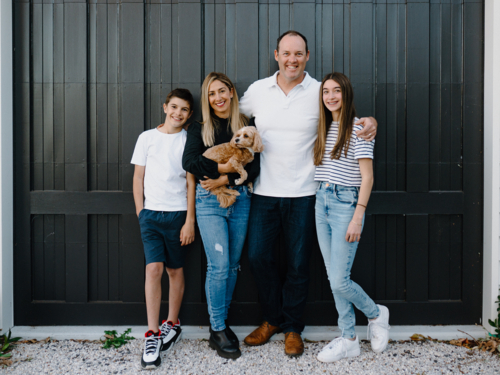 Happy family standing outside in front of black garage door with pet dog - Australian Stock Image