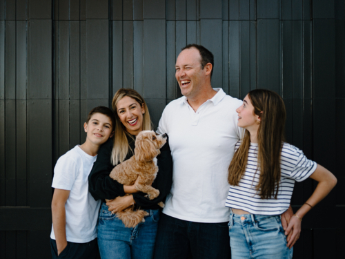 Happy family standing outside in front of black garage door with pet dog - Australian Stock Image