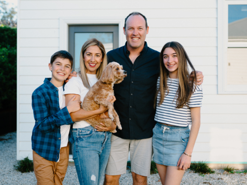 Happy family standing outside their home with their dog. - Australian Stock Image