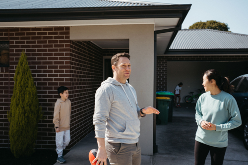 Happy family standing outside their house in the driveway. - Australian Stock Image