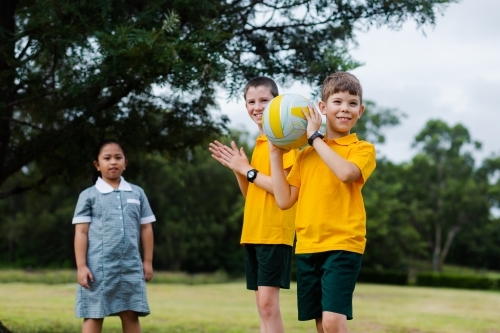 Happy healthy school kids throwing a ball to one another outside - Australian Stock Image