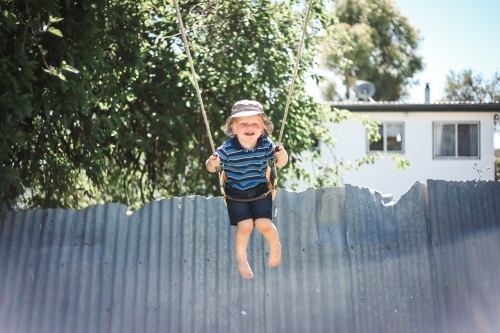 Happy little boy playing on backyard swing - Australian Stock Image