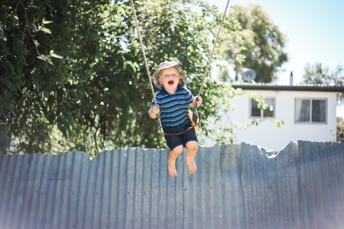 Happy little boy playing on backyard swing - Australian Stock Image