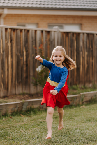 Happy little girl in a superhero costume running around backyard - Australian Stock Image