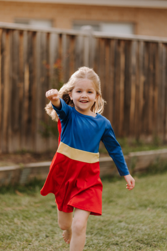 Happy little girl in a superhero costume running around backyard - Australian Stock Image