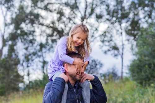 Happy little girl riding on her dads shoulders covering his face - Australian Stock Image