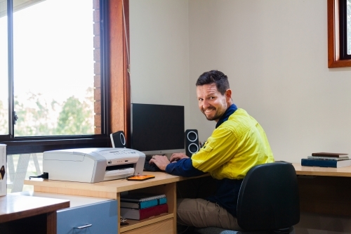 Happy male tradie at computer in home office - Australian Stock Image