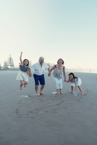 Happy multicultural grandparent with grandchildren on the beach - Australian Stock Image