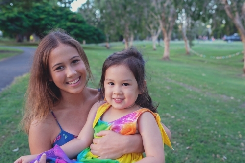 Happy multiethnic teenage girl holding little girl in the park - Australian Stock Image