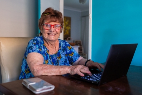 Happy older woman working on laptop at table - Australian Stock Image