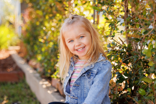 Happy preschool child sitting on edge of garden bed in bright sunny kindergarten yard - Australian Stock Image