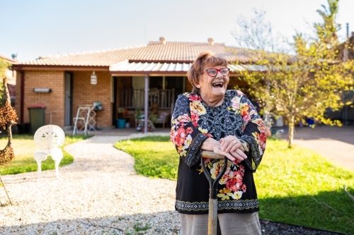 Happy senior woman outside in garden leaning on spade laughing - Australian Stock Image