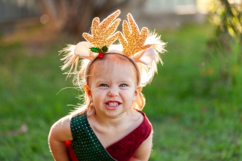 Happy smiling little girl in Christmas colours and wearing deer antler headband - Australian Stock Image