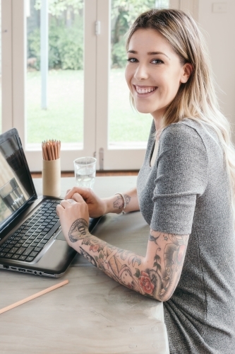 Happy smiling young woman working at home on her dining table - Australian Stock Image