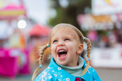 Happy toddler girl portrait at colourful country show event on overcast day - Australian Stock Image