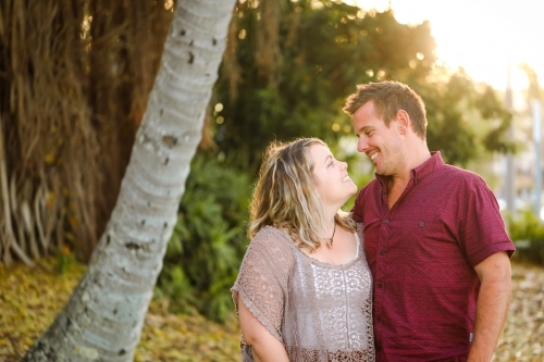 Happy twenty-something couple embracing in golden afternoon light at the park - Australian Stock Image