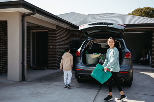 happy woman carrying a reusable shopping bag from the car boot - Australian Stock Image