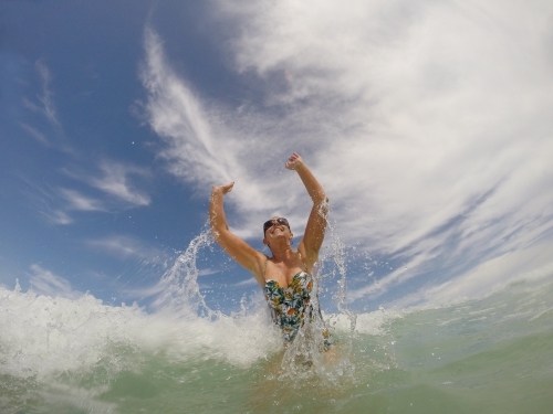 Happy woman jumping up in the waves in the surf - Australian Stock Image