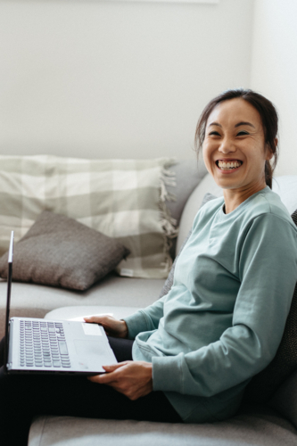 Happy woman sitting on the couch while holding her laptop. - Australian Stock Image