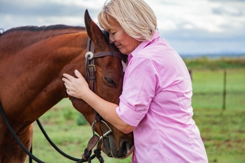 Happy woman standing at her horses head holding bridle - Australian Stock Image