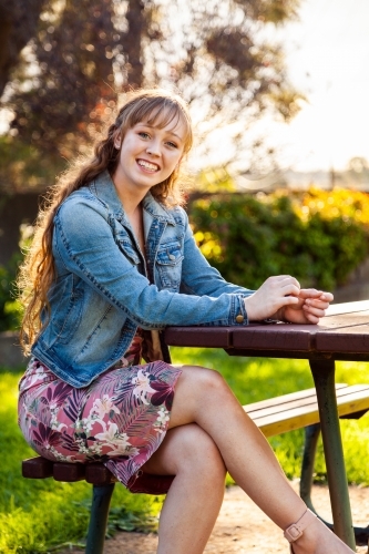 Happy young adult sitting at park bench in autumn - Australian Stock Image