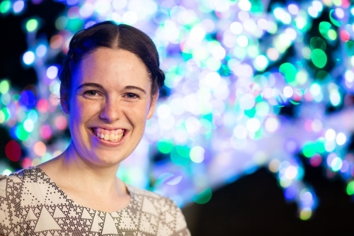 Happy young adult woman smiling during Christmas season with bokeh lights - Australian Stock Image