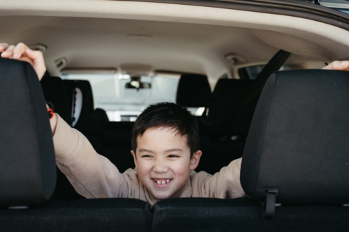 Happy young boy in the backseat of car looking out the back smiling - Australian Stock Image