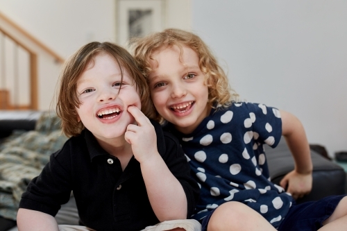 Happy young children smiling while sitting on the couch - Australian Stock Image