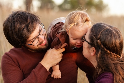 Happy young dad holding toddler girl on shoulder outside at sunset - Australian Stock Image