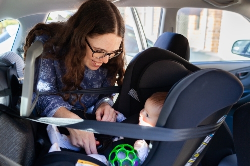 Happy young mum getting baby out of rear facing child car seat - Australian Stock Image