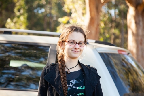 Happy young person standing beside car smiling - Australian Stock Image