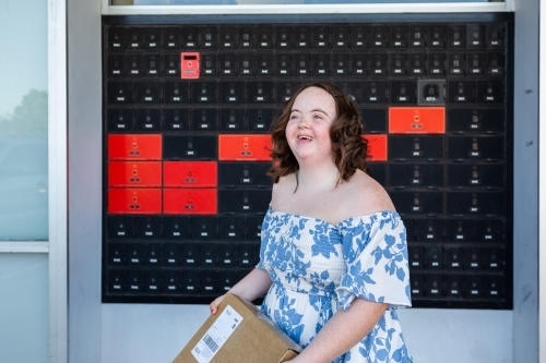 Happy young person with a disability holding brown box parcel near post office - Australian Stock Image