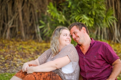 Happy young romantic couple sitting together in golden afternoon light at the park - Australian Stock Image