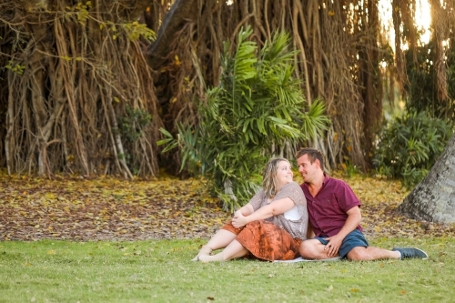 Happy young romantic couple sitting together in golden afternoon light at the park - Australian Stock Image