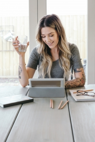 Happy young woman reading a tablet in a light bright home office - Australian Stock Image