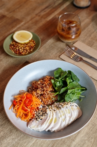 Healthy chicken and salad dish on wooden table in cafe - Australian Stock Image