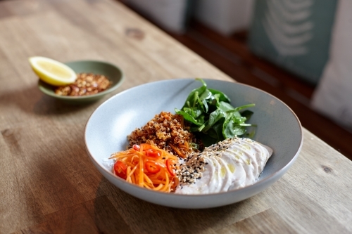 Healthy chicken, salad and grains in bowl on wooden table in cafe - Australian Stock Image