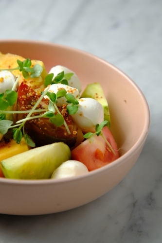 Heirloom tomatoes salad with mozzarella cheese in a pink bowl - Australian Stock Image