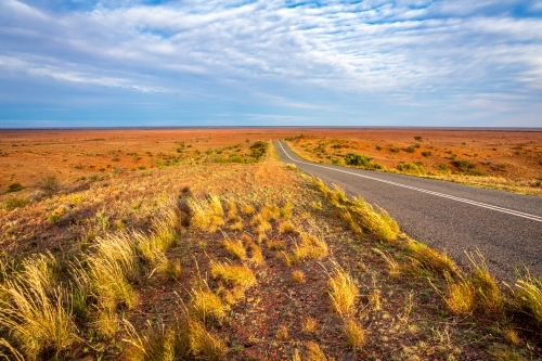 Highway through the desert landscape of outback Australia, rocky red soils, tufted grasses