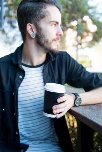 Hipster man sitting outdoors with a take away coffee - Australian Stock Image