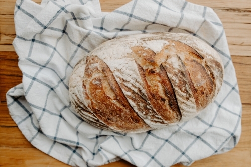 Home made Sour dough bread cooling on a tea towel which is on a wooden chopping platter board - Australian Stock Image