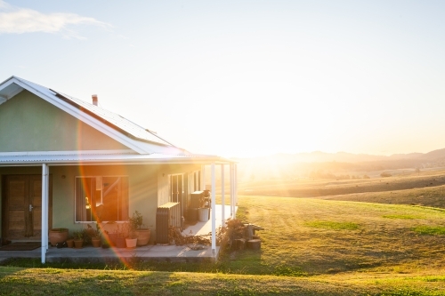 Homestead on hilltop with last rays of sunlight shining over scene and solar panels on roof - Australian Stock Image