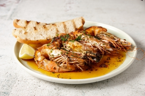 horizontal close up shot of sautéed shrimps with a slice of lemon and some toast in the side - Australian Stock Image