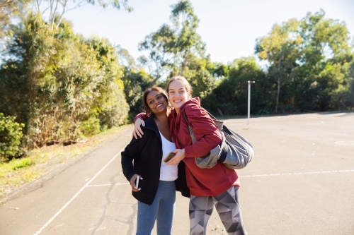 horizontal photo of two young women wearing coat and jacket close to each other on a sunny day - Australian Stock Image