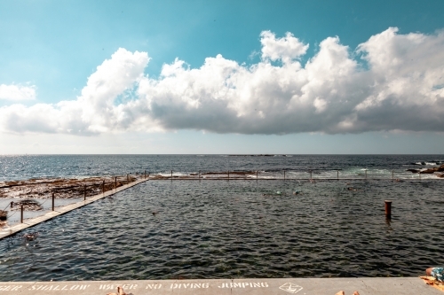 horizontal shot of a beach pool with people swimming on a sunny day - Australian Stock Image