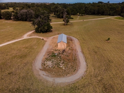 horizontal shot of a farmhouse with a road around it and with trees in the background under blue sky - Australian Stock Image