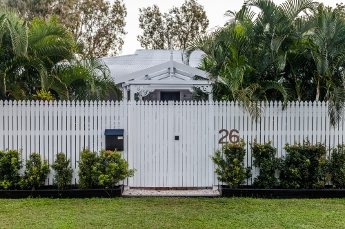 horizontal shot of a house with white fence, grass, bushes and trees - Australian Stock Image